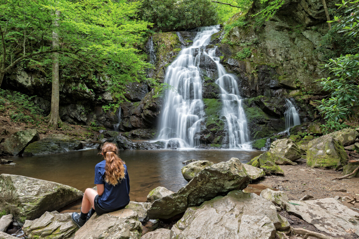 Woman sits by a waterfall in the Great Smoky Mountains
